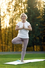 Image of Mature woman practicing yoga on green grass in park
