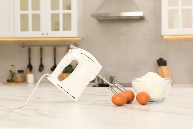 Photo of Modern mixer, eggs and bowl with flour on white marble table in kitchen