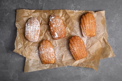 Photo of Delicious madeleine cakes with powdered sugar on grey table, flat lay