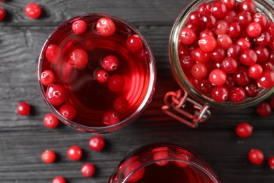 Photo of Tasty cranberry juice in glasses and fresh berries on black wooden table, flat lay