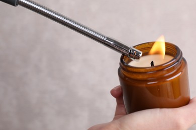 Woman lighting candle with gas lighter against grey wall, closeup