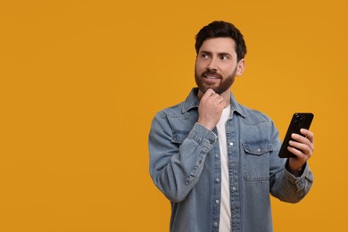 Smiling man with smartphone on orange background. Space for text