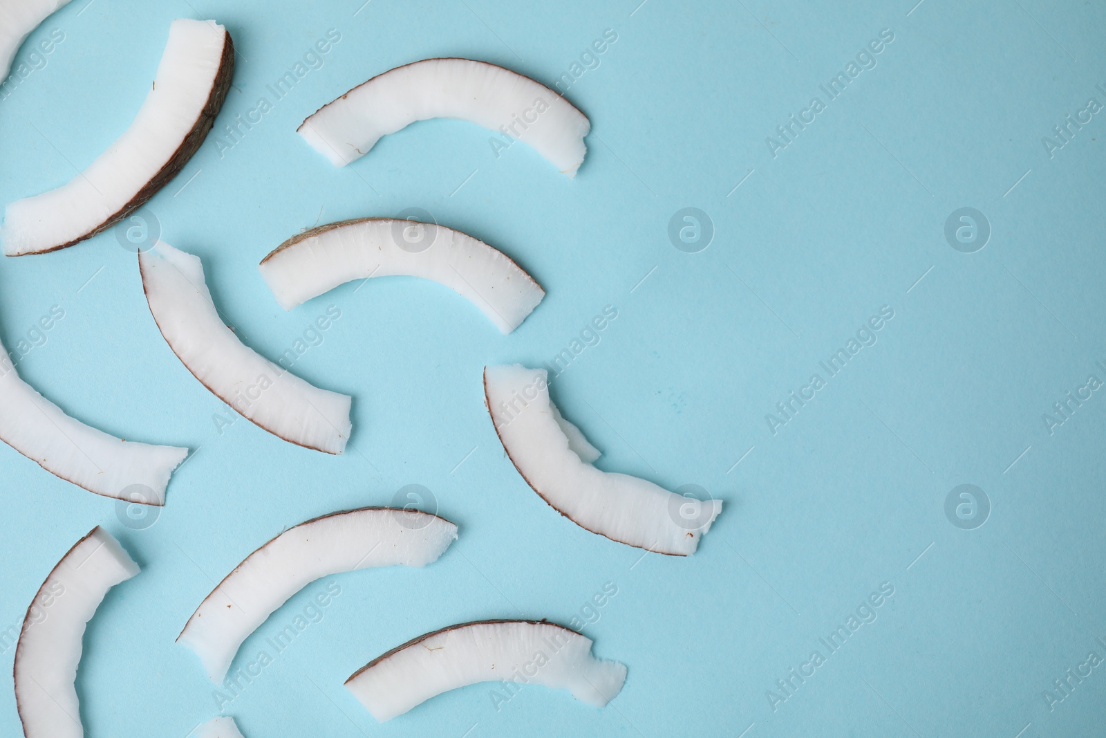 Photo of Fresh coconut pieces on light blue background, top view. Space for text