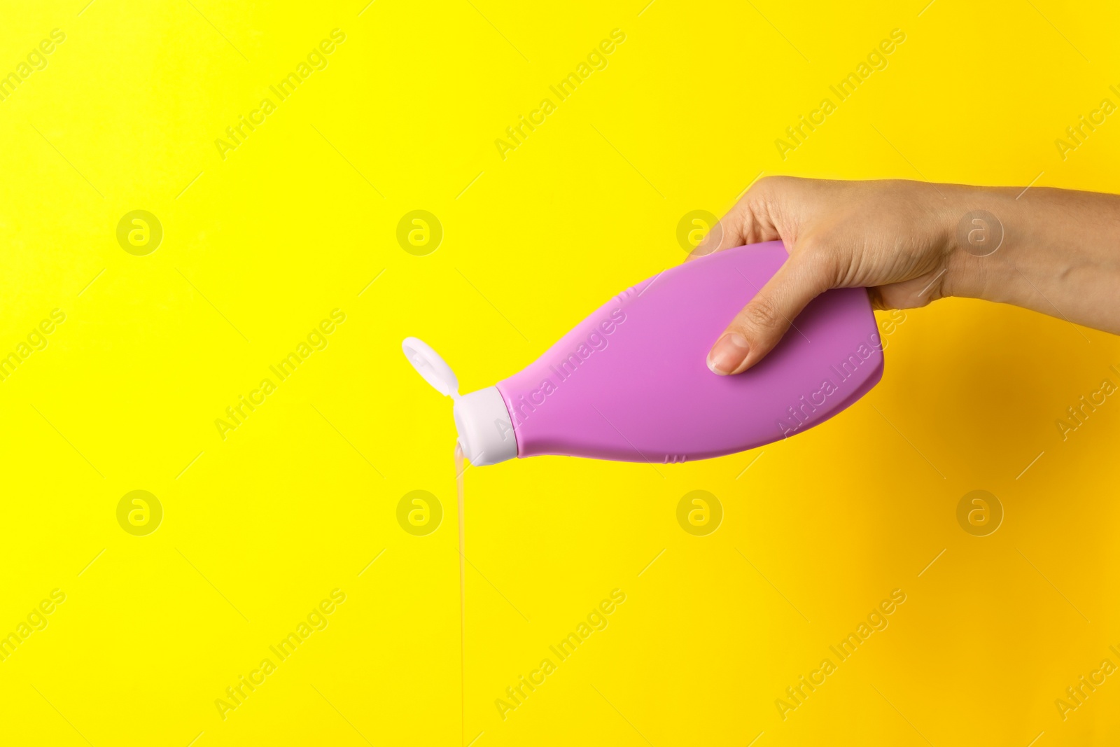 Photo of Woman pouring cosmetic product from bottle on yellow background, closeup. Space for text