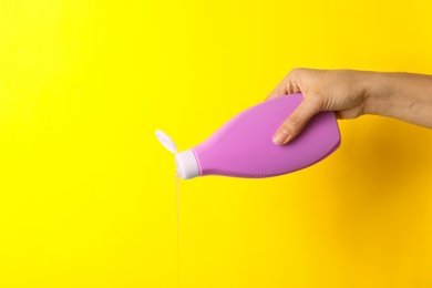 Woman pouring cosmetic product from bottle on yellow background, closeup. Space for text