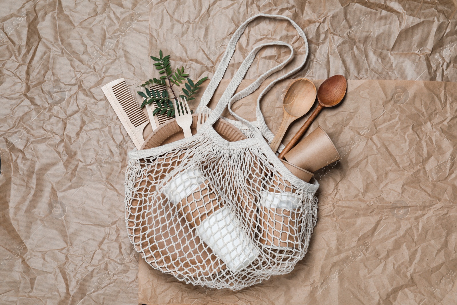 Photo of Net bag with different eco items on crumpled paper, top view. Recycling concept