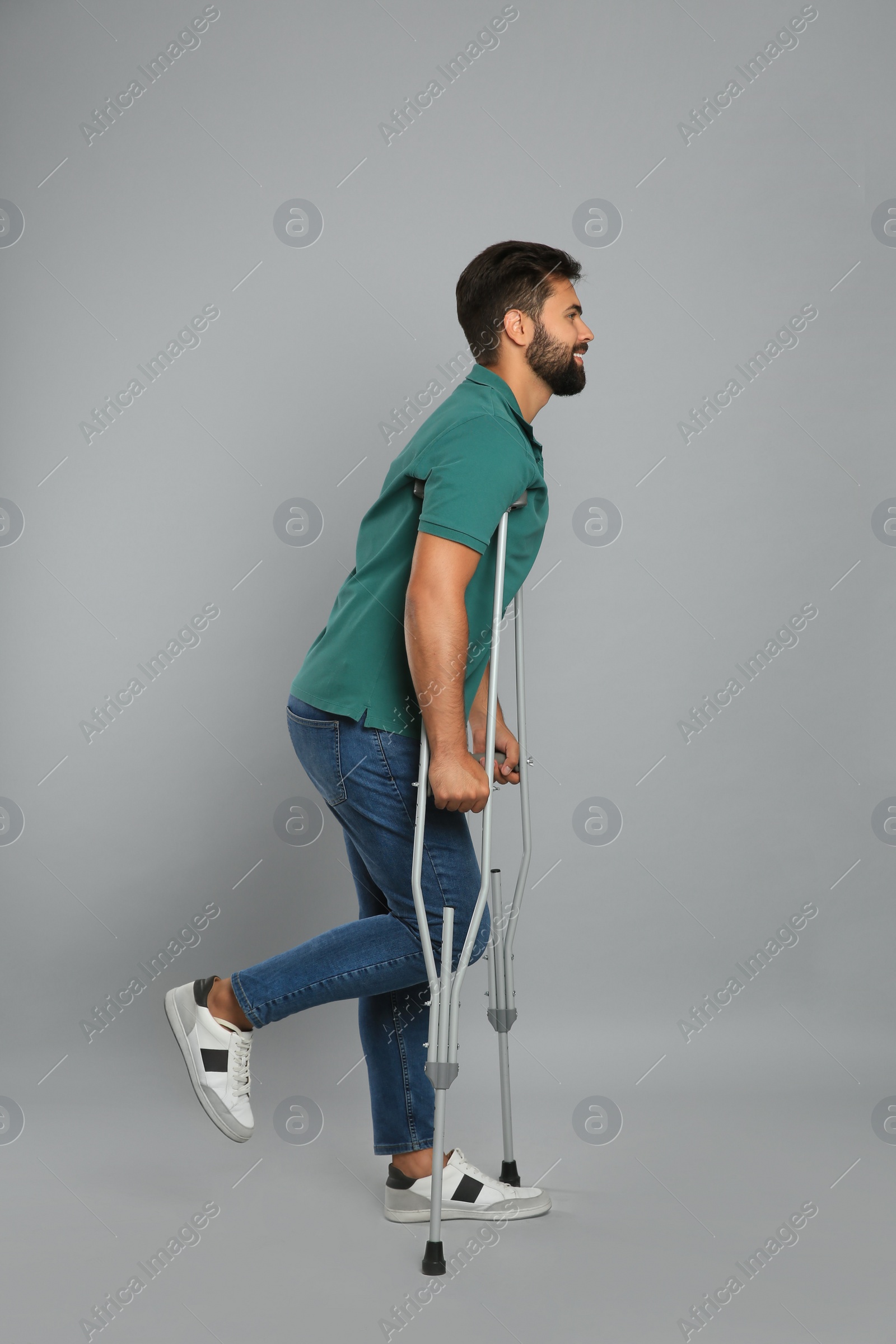 Photo of Young man with axillary crutches on grey background