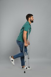 Young man with axillary crutches on grey background