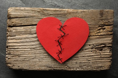 Photo of Broken heart. Torn red paper heart sewed with thread on grey table, top view