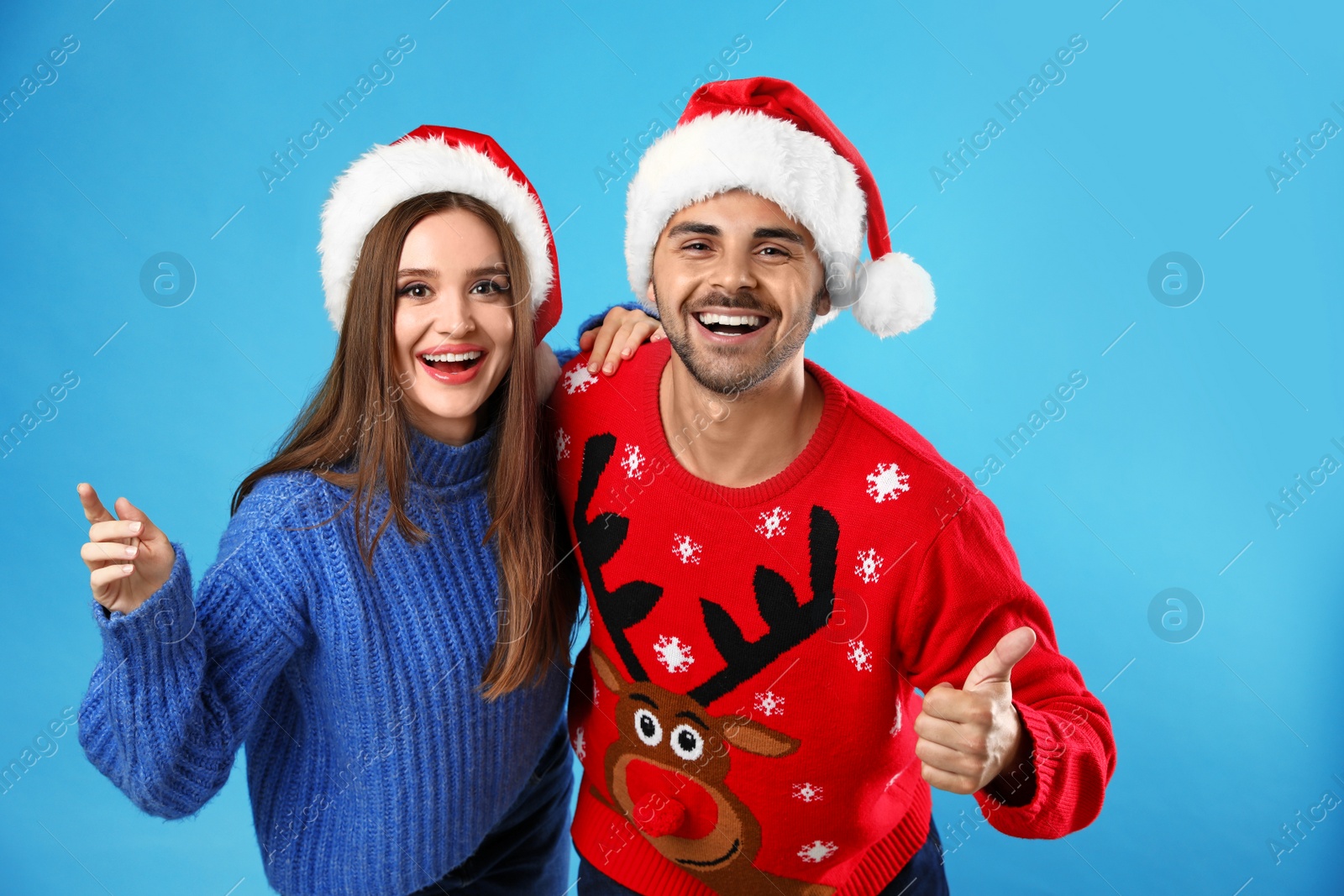 Photo of Couple wearing Christmas sweaters and Santa hats on blue background