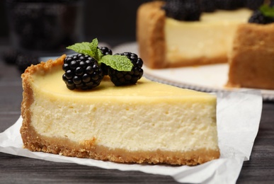 Photo of Piece of delicious cheesecake decorated with blackberries on table