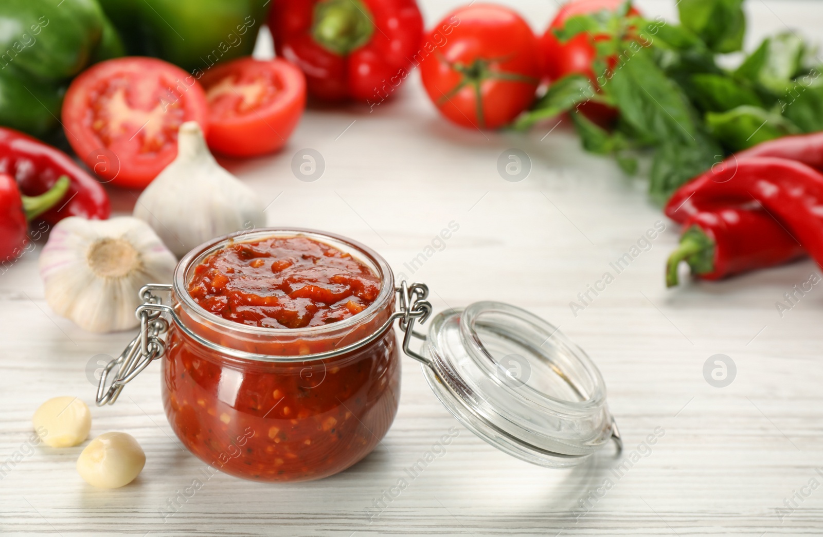 Photo of Glass jar of tasty adjika and ingredients on white wooden table, space for text