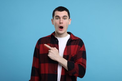 Surprised man pointing at something on light blue background