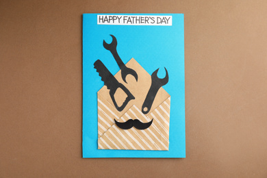 Photo of Greeting card with phrase HAPPY FATHER'S DAY on brown background, top view