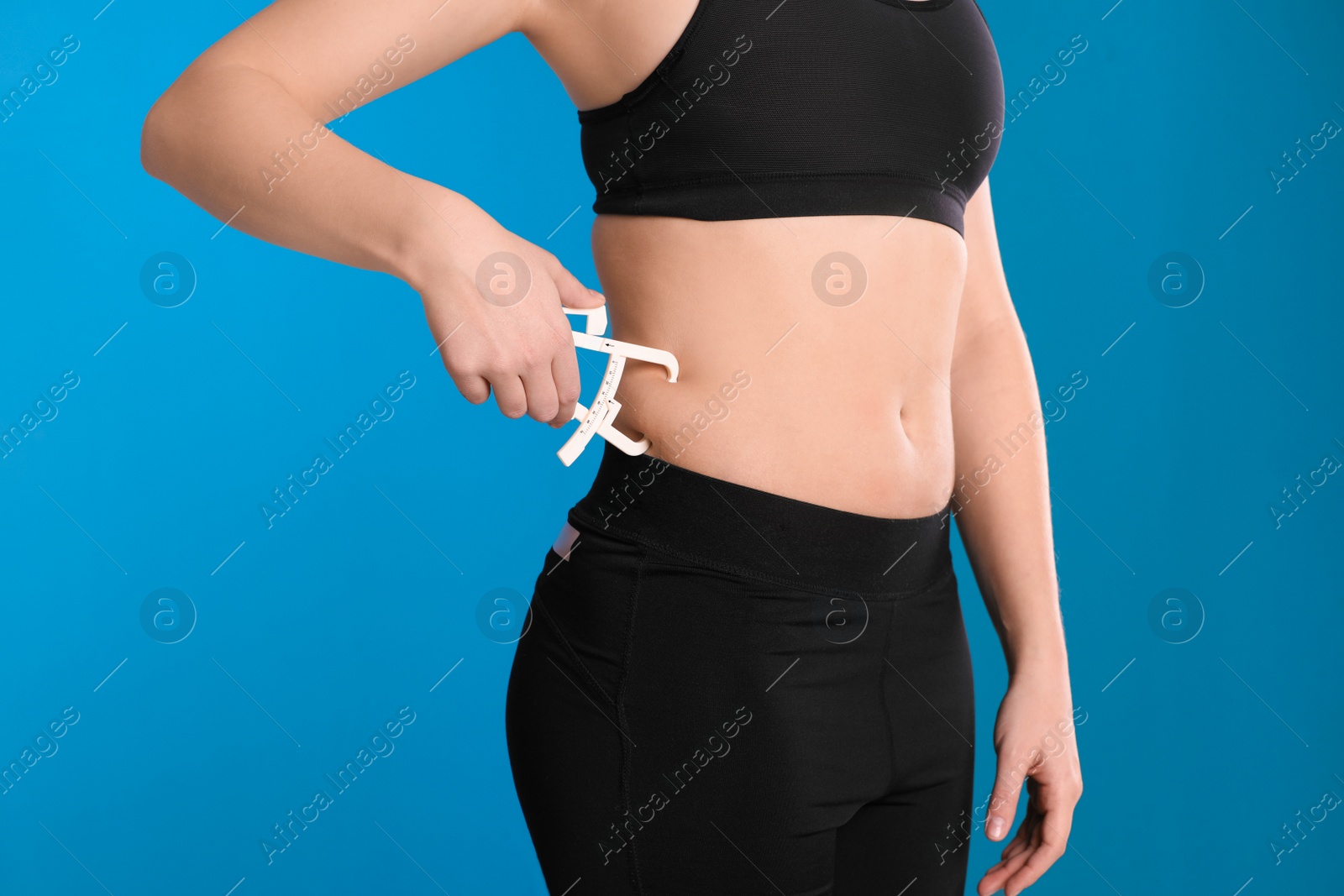 Photo of Young woman measuring body fat with caliper on blue background, closeup. Nutritionist's tool