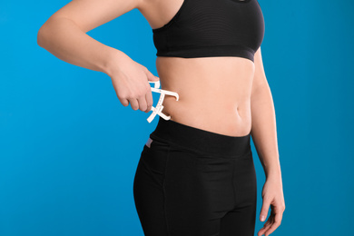 Photo of Young woman measuring body fat with caliper on blue background, closeup. Nutritionist's tool