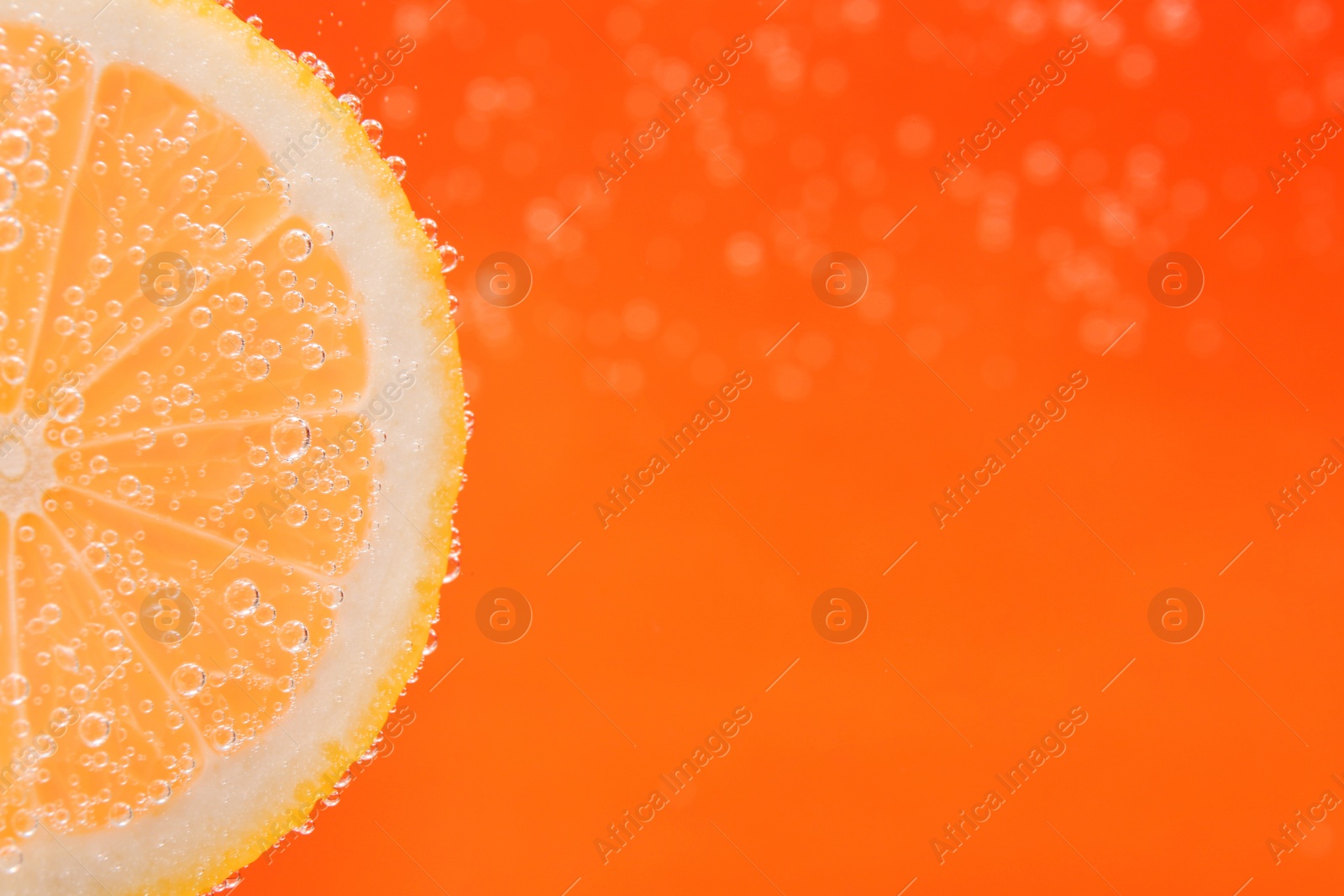 Photo of Slice of lemon in sparkling water on orange background, closeup with space for text. Citrus soda