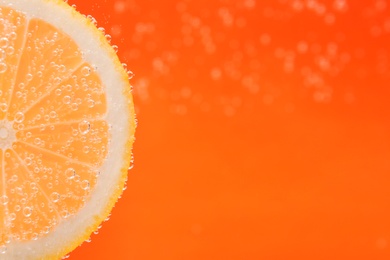 Photo of Slice of lemon in sparkling water on orange background, closeup with space for text. Citrus soda