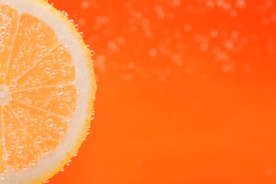 Slice of lemon in sparkling water on orange background, closeup with space for text. Citrus soda