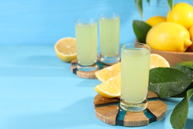 Photo of Tasty limoncello liqueur, lemons and green leaves on light blue table, space for text