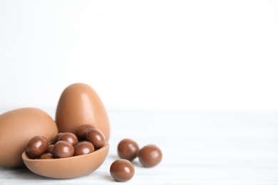 Photo of Whole and broken chocolate eggs with candies on white wooden table, space for text