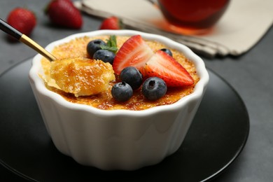 Taking delicious creme brulee with berries from bowl at grey table, closeup
