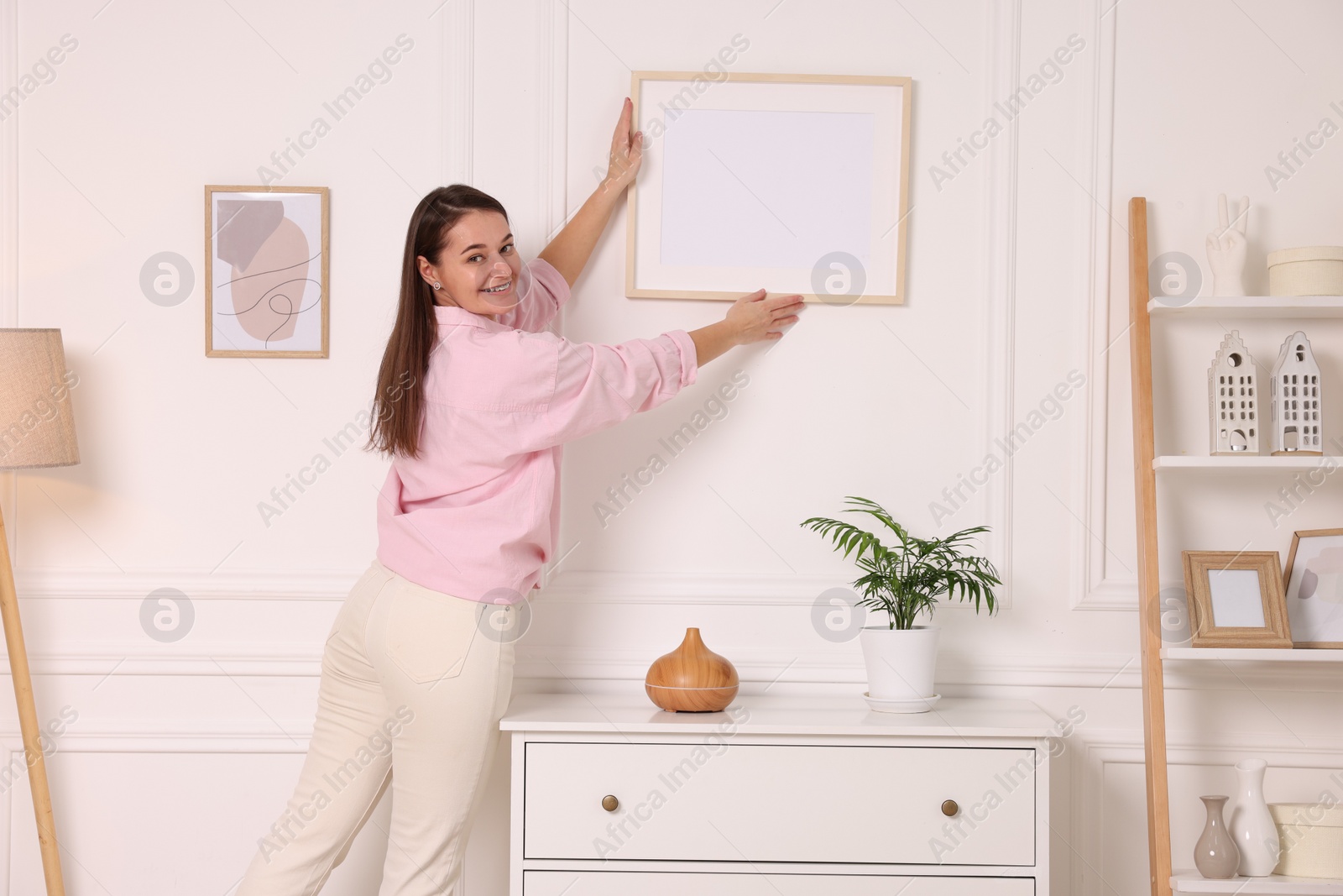 Photo of Woman hanging picture frame on white wall at home