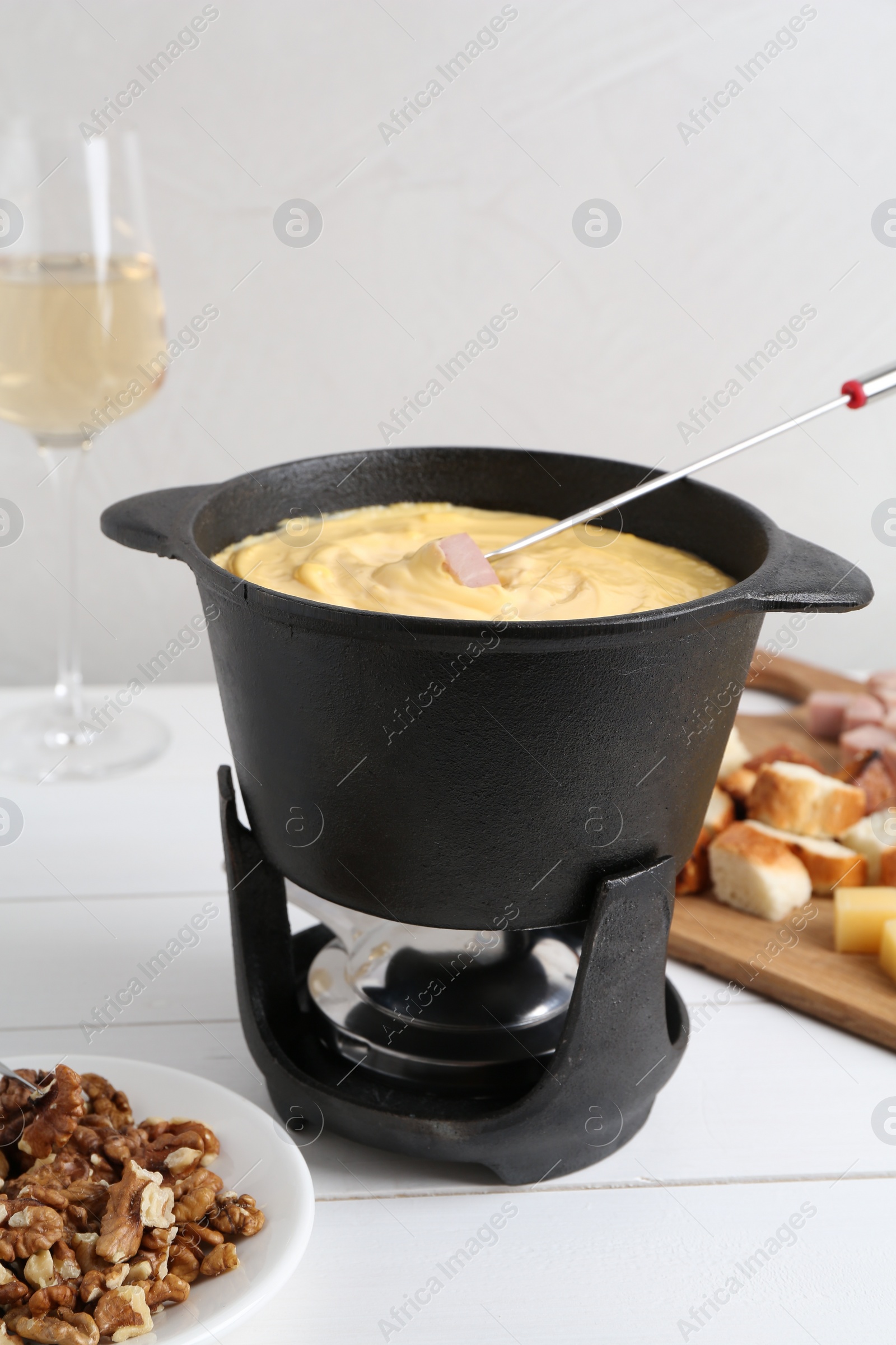 Photo of Fondue pot with tasty melted cheese, fork and different snacks on white wooden table