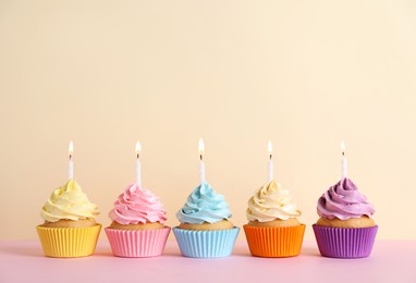 Photo of Delicious birthday cupcakes with burning candles on pink table against beige background