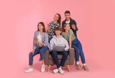 Photo of Group of happy teenagers using laptop and smartphones on light pink background