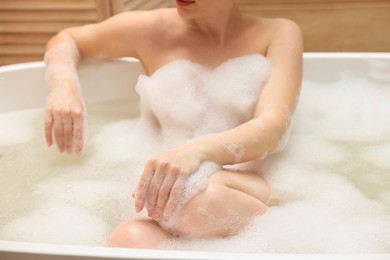 Photo of Woman taking bath with foam in tub indoors, closeup