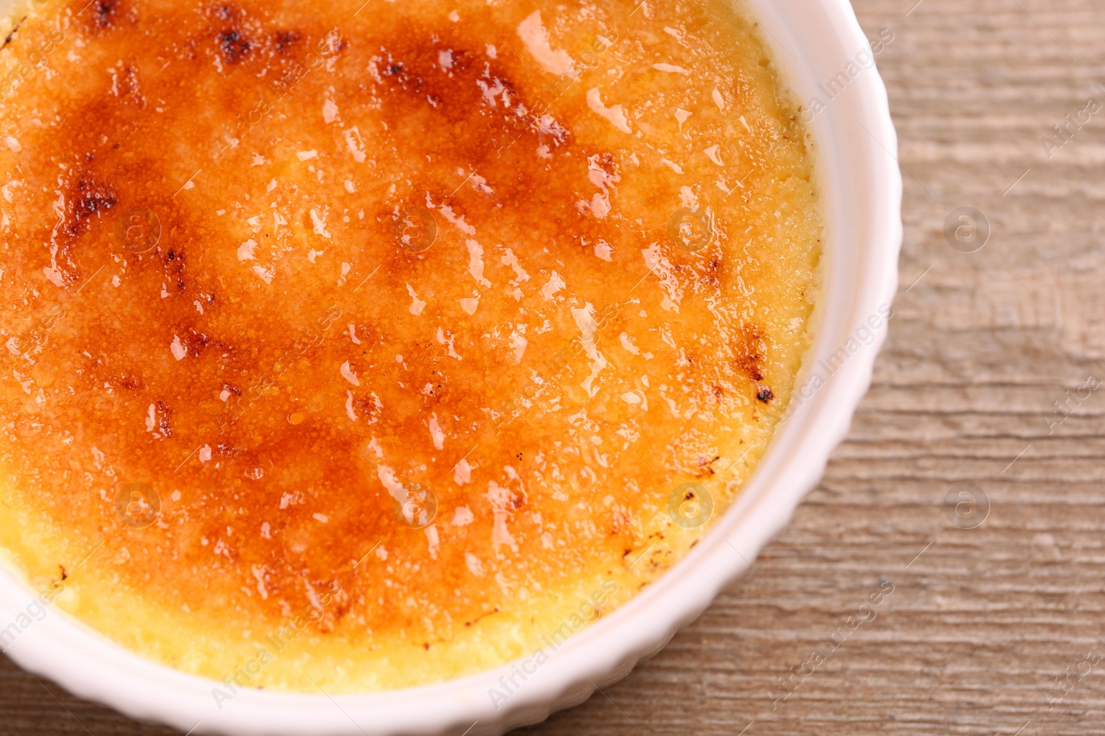 Photo of Delicious creme brulee in bowl on wooden table, top view