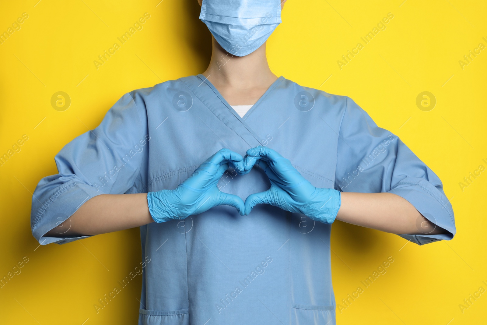 Photo of Doctor making heart with hands on yellow background, closeup