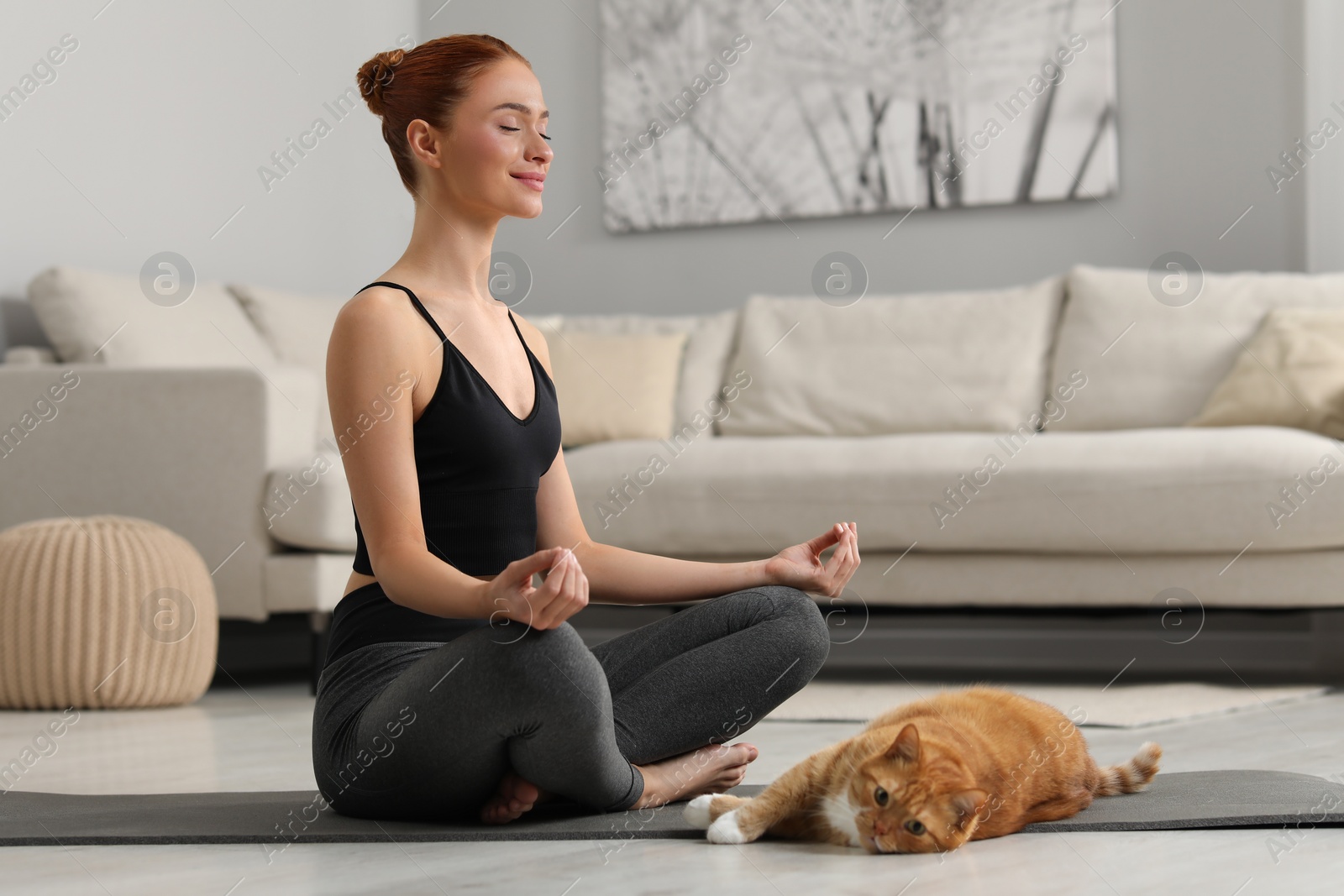 Photo of Beautiful woman with cute red cat practicing yoga on mat at home