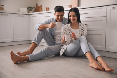 Photo of Happy couple sitting on warm floor in kitchen. Heating system