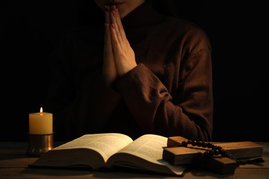 Woman praying at table with burning candle and Bible, closeup