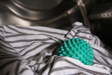 Green dryer ball and clothes in washing machine drum, closeup. Space for text