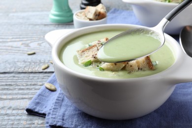 Photo of Spoon with delicious asparagus soup over bowl on grey wooden table, closeup