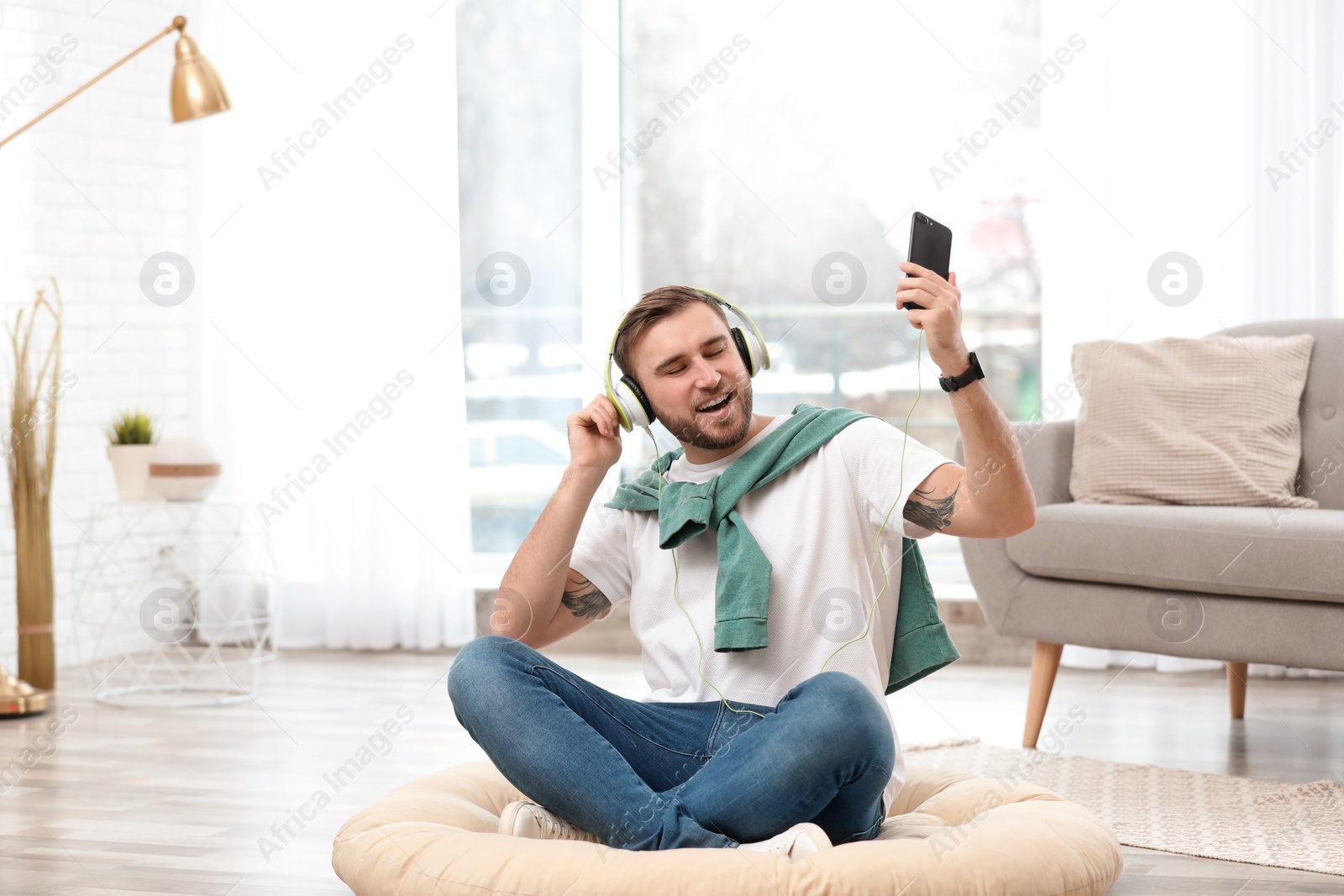 Photo of Young man with headphones and mobile device enjoying music on floor in living room