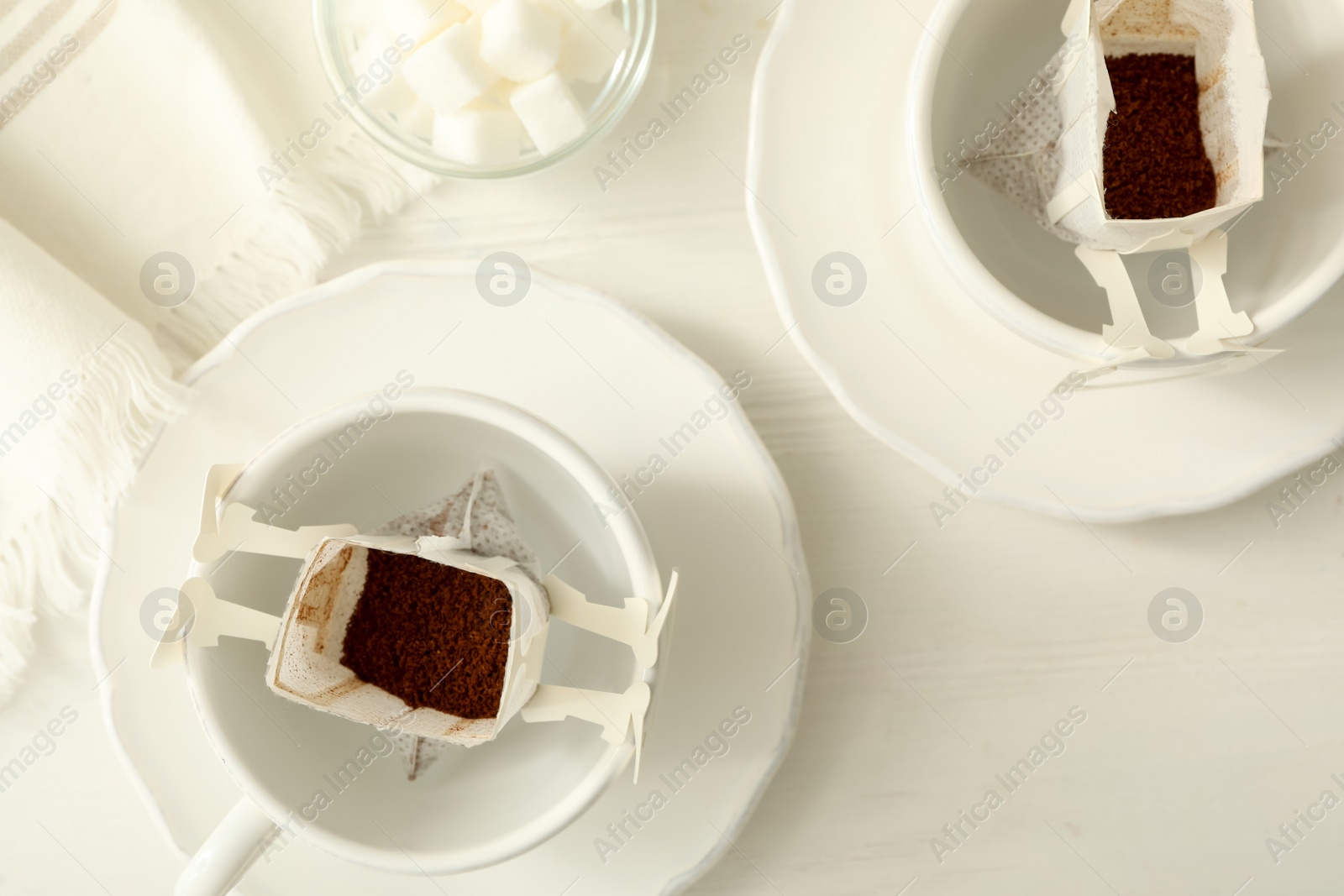 Photo of Cups with drip coffee bags on white wooden table, flat lay