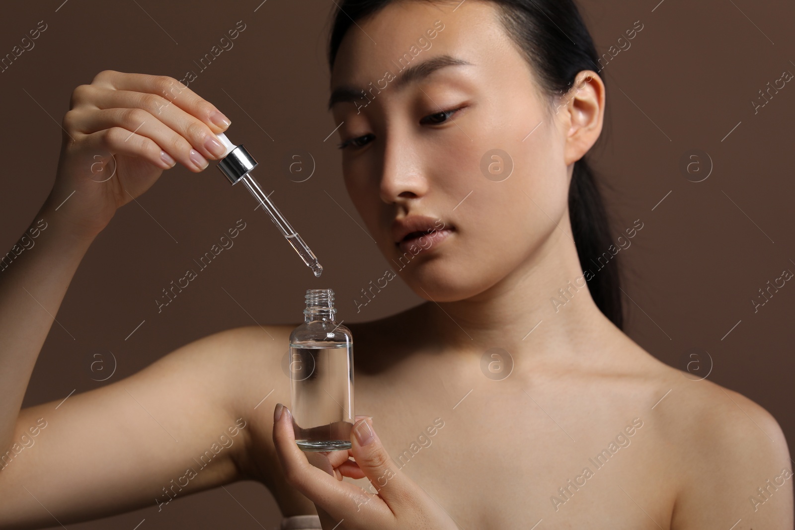Photo of Beautiful young woman with bottle of cosmetic serum on brown background, closeup