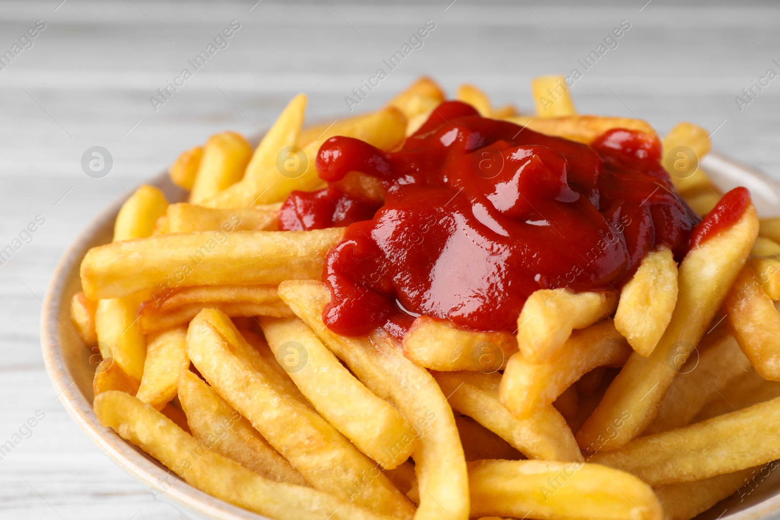 Photo of Bowl of tasty french fries on white wooden table, closeup