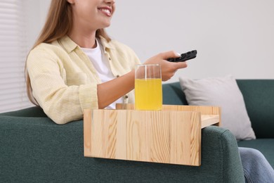Glass of juice on sofa armrest wooden table. Woman changing TV channels at home, closeup