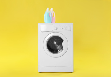 Modern washing machine with detergents on yellow background. Laundry day