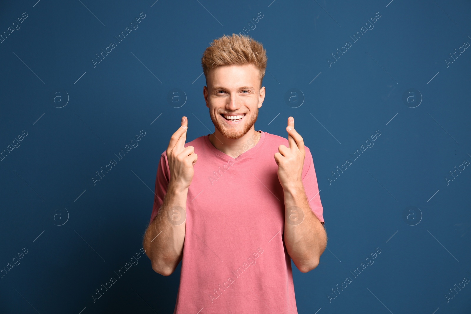Photo of Portrait of hopeful man with crossed fingers on blue background