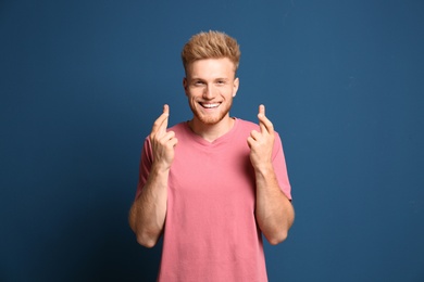 Portrait of hopeful man with crossed fingers on blue background