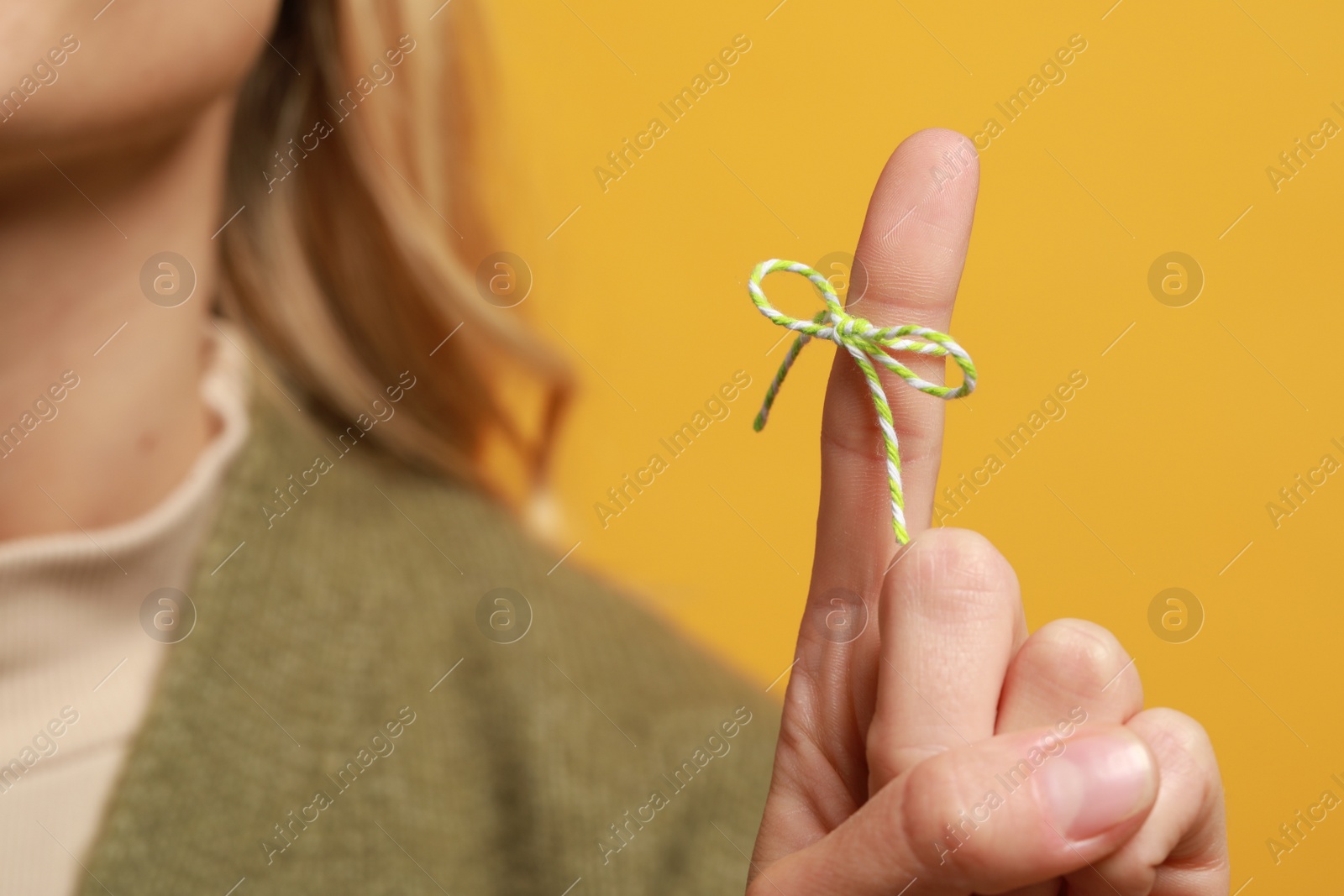 Photo of Woman showing index finger with tied bow as reminder against orange background, focus on hand