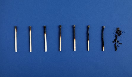 Different stages of burnt matches on blue background, flat lay