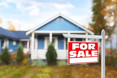 Sale sign near beautiful house outdoors. Red signboard with words