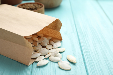 Photo of Paper bag with raw pumpkin seeds on blue wooden table, closeup. Vegetable planting